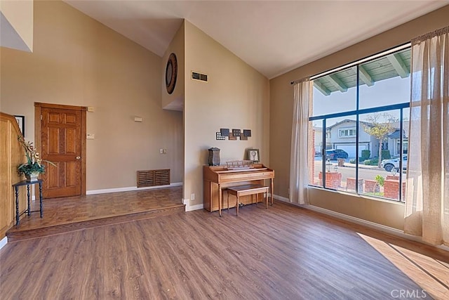 interior space featuring visible vents, baseboards, high vaulted ceiling, and wood finished floors