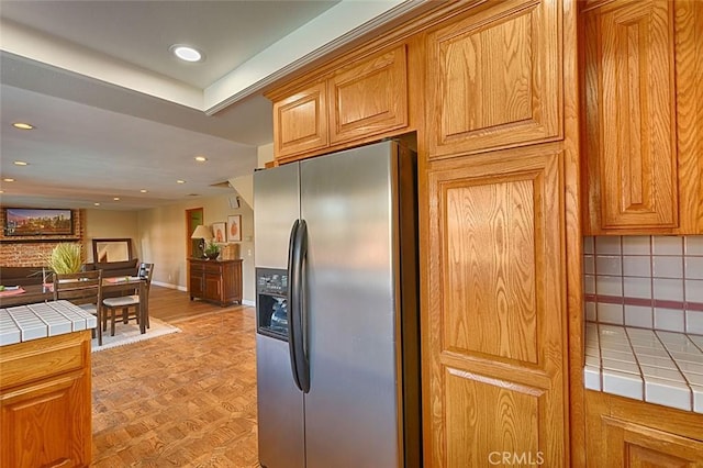 kitchen with recessed lighting, stainless steel fridge, tile counters, and brown cabinetry