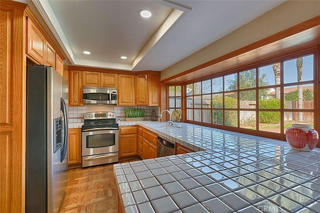 kitchen featuring backsplash, tile counters, a tray ceiling, stainless steel appliances, and a sink