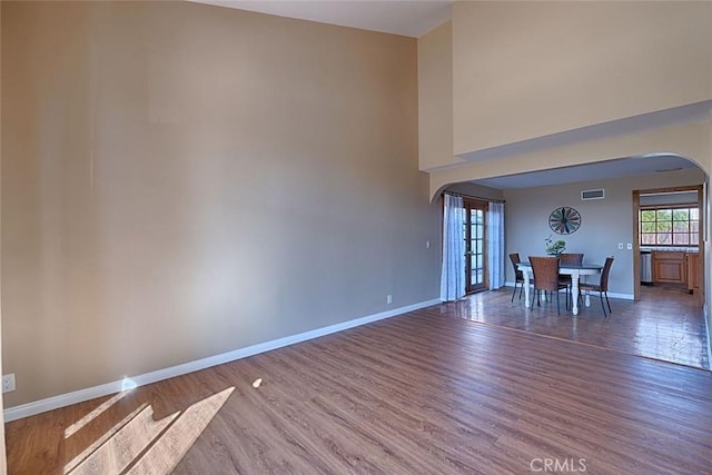 unfurnished room featuring arched walkways, visible vents, baseboards, and wood finished floors