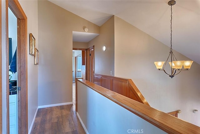 hallway with baseboards, an inviting chandelier, vaulted ceiling, dark wood-type flooring, and an upstairs landing