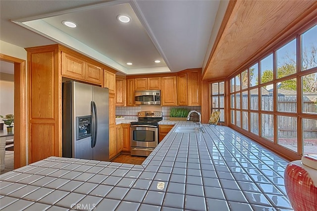 kitchen with a sink, stainless steel appliances, a wealth of natural light, and tile counters