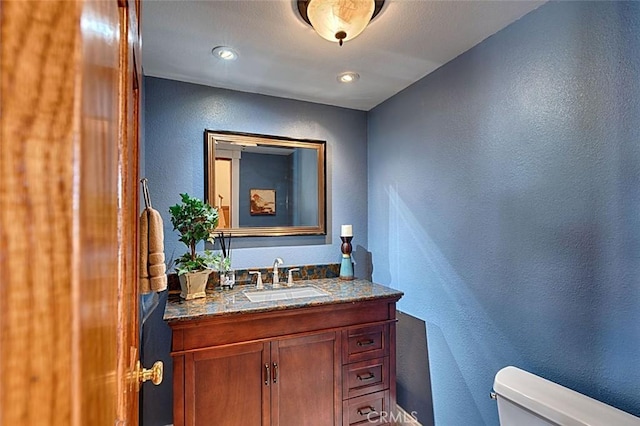 bathroom featuring toilet, vanity, and a textured wall