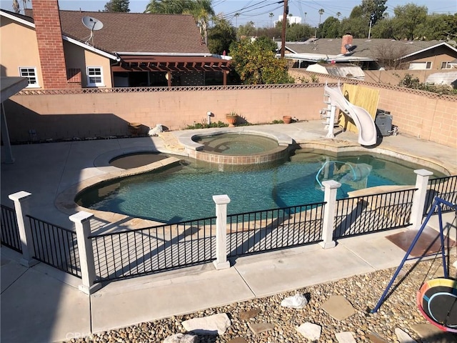 view of swimming pool with a water slide, fence, and a pool with connected hot tub