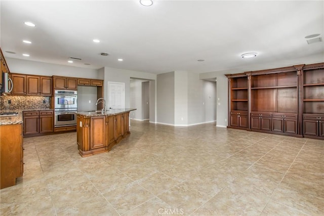60310 Desert Rose Dr, La Quinta, CA 92253 - kitchen featuring appliances with stainless steel finishes, light stone countertops, brown cabinetry, a sink, and backsplash