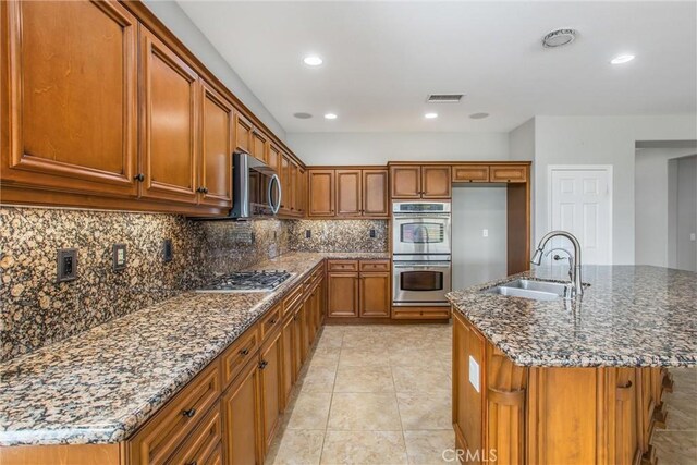 60310 Desert Rose Dr, La Quinta, CA 92253 - kitchen with a sink, appliances with stainless steel finishes, brown cabinetry, dark stone countertops, and decorative backsplash