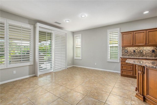 60310 Desert Rose Dr, La Quinta, CA 92253 - kitchen featuring brown cabinets, light tile patterned floors, backsplash, dark stone countertops, and baseboards