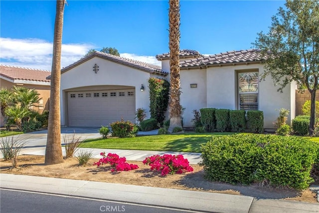 mediterranean / spanish-style home with a tile roof, stucco siding, concrete driveway, an attached garage, and a front yard