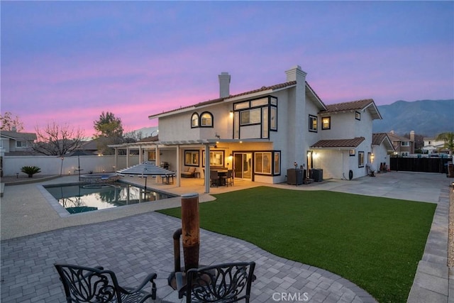 back of house at dusk with a fenced in pool, a yard, a patio area, a pergola, and a fenced backyard