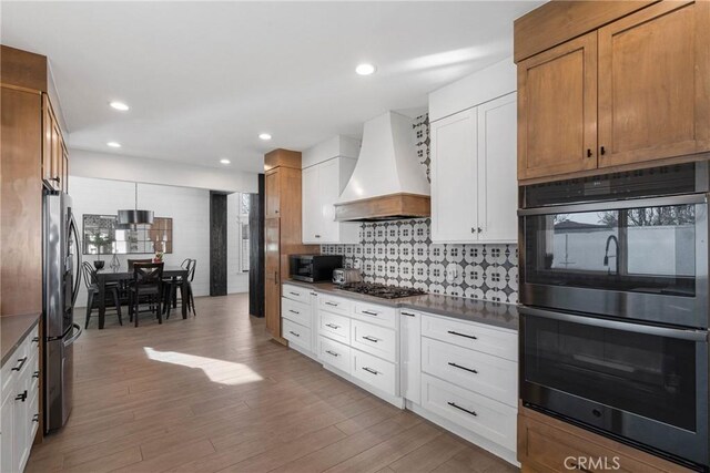 14201 Ross Ct, Rancho Cucamonga, CA 91739 - kitchen with appliances with stainless steel finishes, premium range hood, backsplash, light wood-style floors, and dark countertops