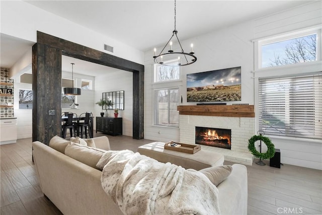 living area with a brick fireplace, visible vents, a towering ceiling, and light wood finished floors