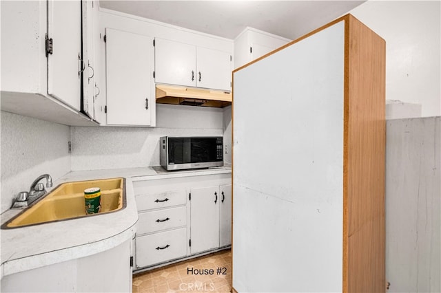 kitchen featuring light countertops, stainless steel microwave, white cabinetry, a sink, and under cabinet range hood