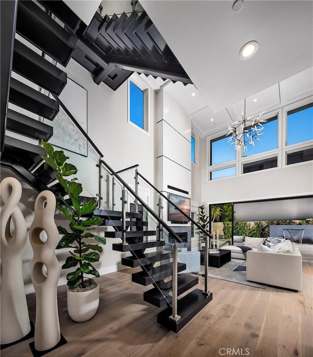 stairway with an inviting chandelier, recessed lighting, wood finished floors, and a towering ceiling