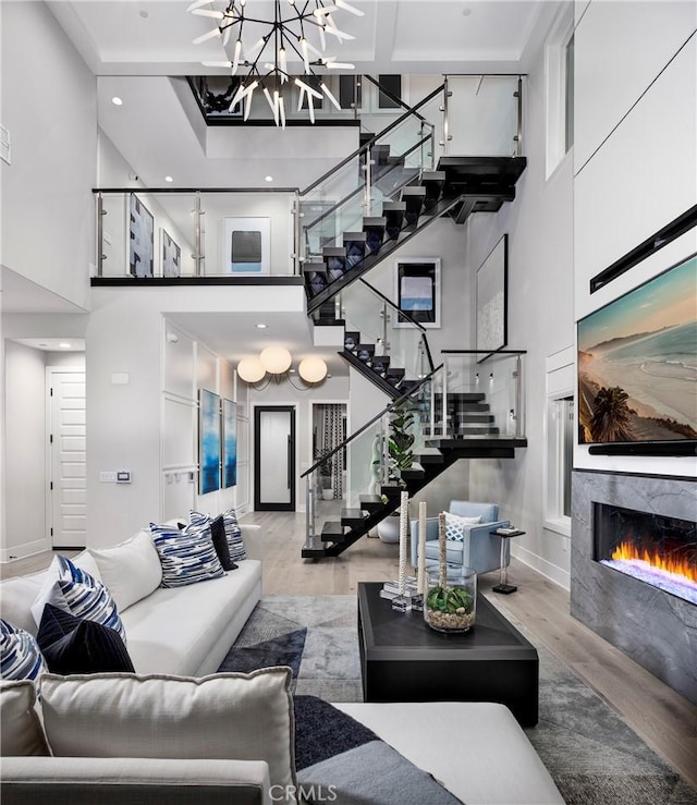 living area featuring baseboards, stairs, a lit fireplace, a high ceiling, and wood finished floors