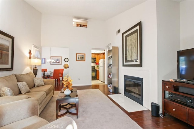 living room with dark wood finished floors, a fireplace with flush hearth, visible vents, and a towering ceiling