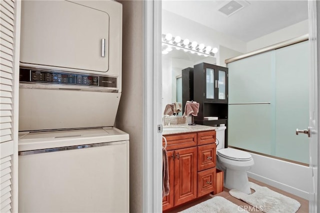 bathroom with toilet, stacked washing maching and dryer, bath / shower combo with glass door, and vanity
