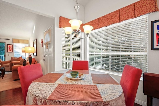 dining area with an inviting chandelier, vaulted ceiling, and wood finished floors
