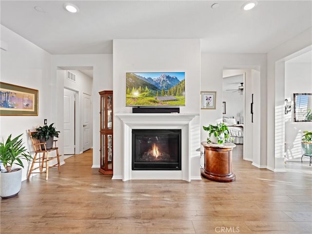 living room featuring light wood-type flooring, visible vents, a glass covered fireplace, and recessed lighting