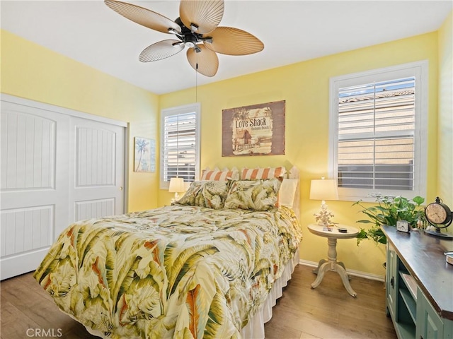 bedroom featuring a ceiling fan, a closet, light wood-style flooring, and baseboards