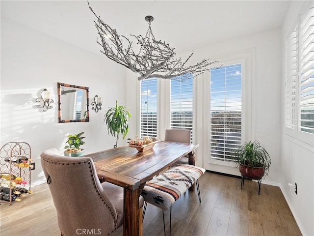 dining area with baseboards, an inviting chandelier, wood finished floors, and a healthy amount of sunlight