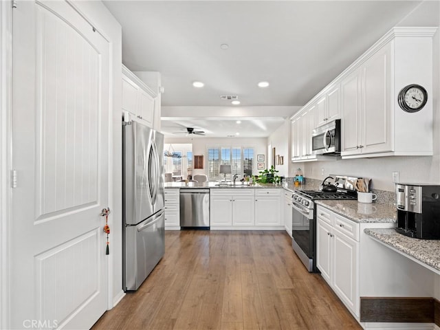 kitchen featuring stainless steel appliances, light stone counters, a sink, and white cabinets