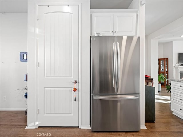 kitchen with dark wood-type flooring, freestanding refrigerator, white cabinets, and light stone counters