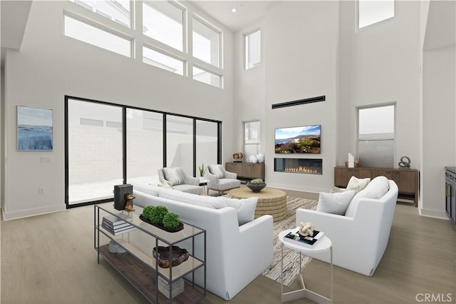 living room featuring light wood-style flooring, a healthy amount of sunlight, a towering ceiling, and baseboards