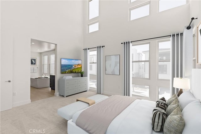 carpeted bedroom with ensuite bath, a high ceiling, and baseboards