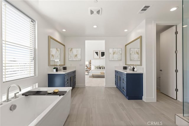 bathroom featuring a soaking tub, a wealth of natural light, visible vents, and a sink
