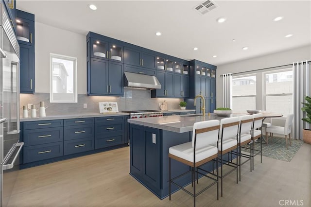 kitchen with visible vents, under cabinet range hood, light wood-style floors, and blue cabinetry