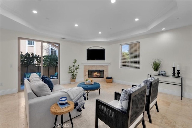 living room featuring recessed lighting, a tiled fireplace, a raised ceiling, and a healthy amount of sunlight