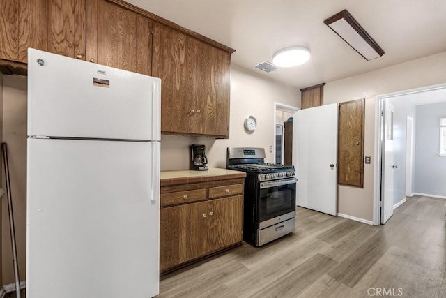 kitchen featuring stainless steel gas range oven, visible vents, tile counters, freestanding refrigerator, and light wood finished floors