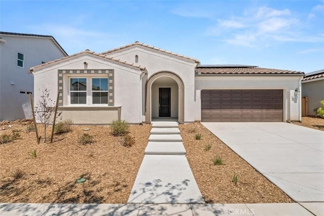 mediterranean / spanish house featuring concrete driveway, an attached garage, a tile roof, and stucco siding