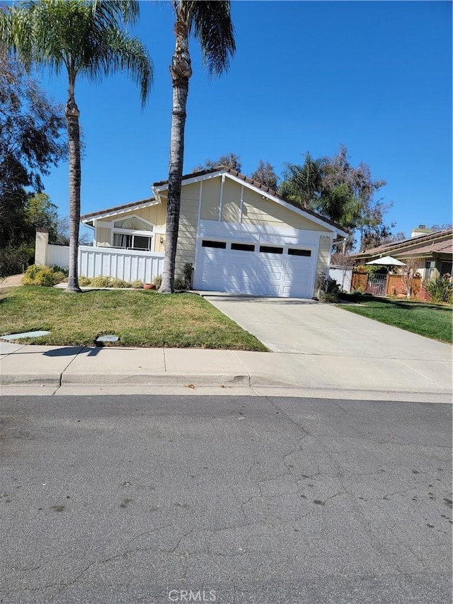 mid-century home featuring driveway, a front lawn, an attached garage, and fence