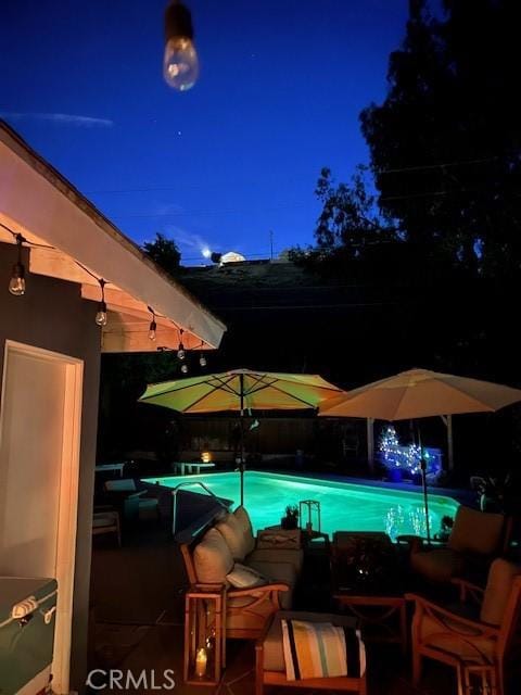 pool at night featuring a patio area and an outdoor pool