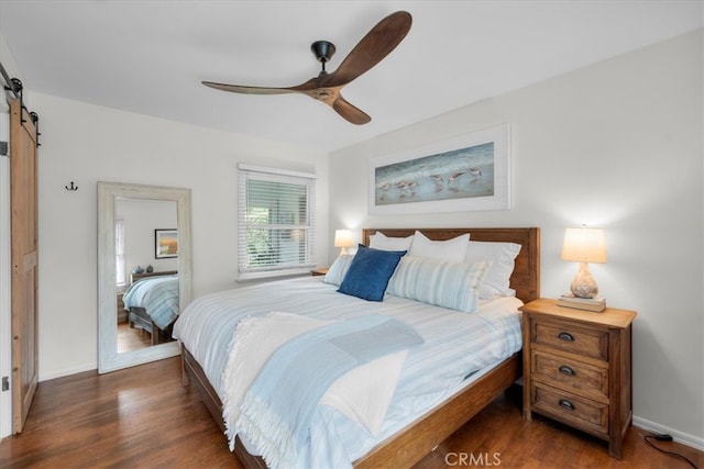 bedroom with ceiling fan, a barn door, dark wood-type flooring, and baseboards