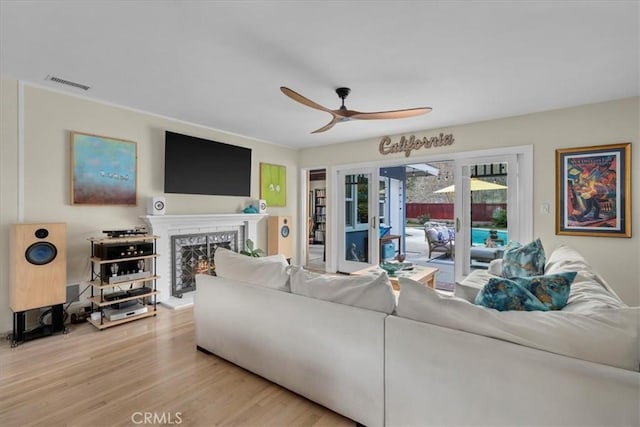 living area with a warm lit fireplace, a ceiling fan, visible vents, and wood finished floors