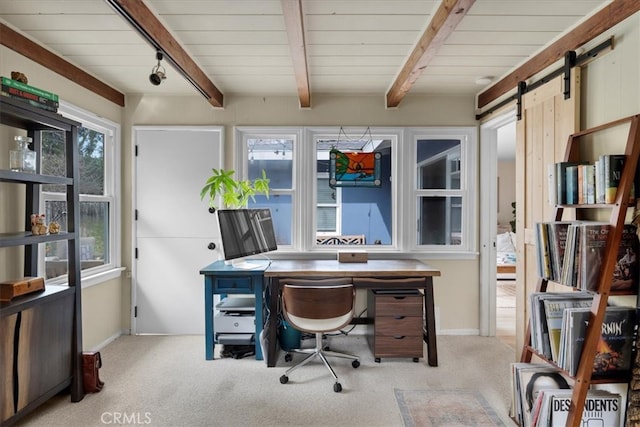 carpeted office space featuring rail lighting, a barn door, baseboards, and beam ceiling