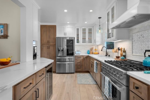 kitchen with beverage cooler, wall chimney exhaust hood, stainless steel appliances, pendant lighting, and a sink