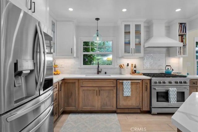 kitchen with ornamental molding, stainless steel appliances, wall chimney range hood, pendant lighting, and a sink