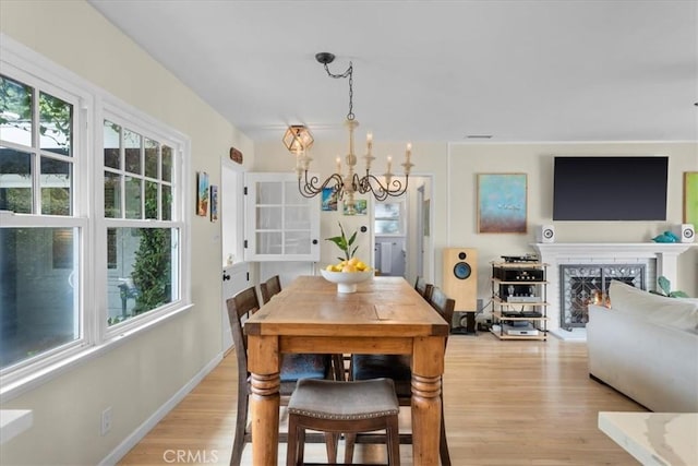 dining space with a chandelier, baseboards, a lit fireplace, and light wood finished floors