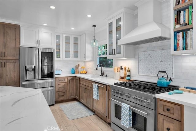 kitchen featuring premium range hood, a sink, white cabinetry, appliances with stainless steel finishes, and pendant lighting