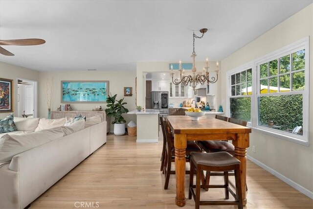 dining space with ceiling fan with notable chandelier, light wood finished floors, and baseboards