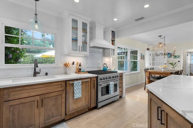 kitchen with a sink, visible vents, wall chimney range hood, high end stainless steel range, and paneled dishwasher