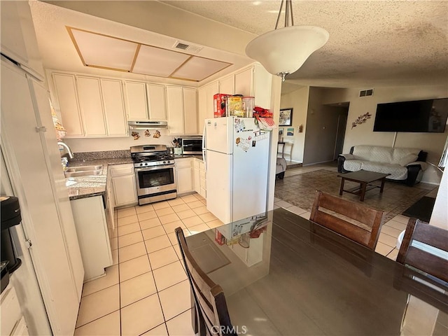 kitchen featuring a sink, white cabinetry, hanging light fixtures, freestanding refrigerator, and gas range