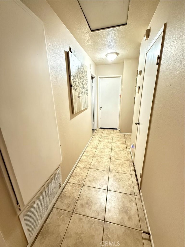 hall featuring a textured ceiling, light tile patterned floors, visible vents, and baseboards