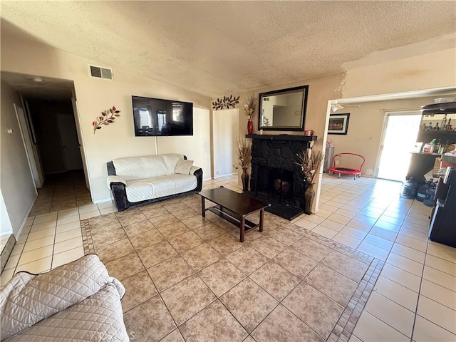 living room featuring a textured ceiling, a stone fireplace, visible vents, and tile patterned floors