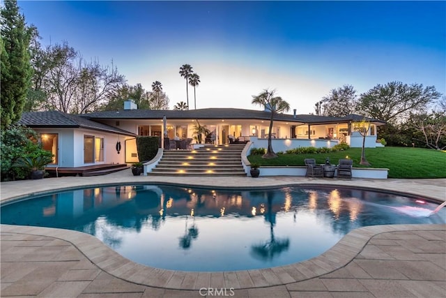 pool at dusk with stairs, an outdoor pool, a patio, and a yard