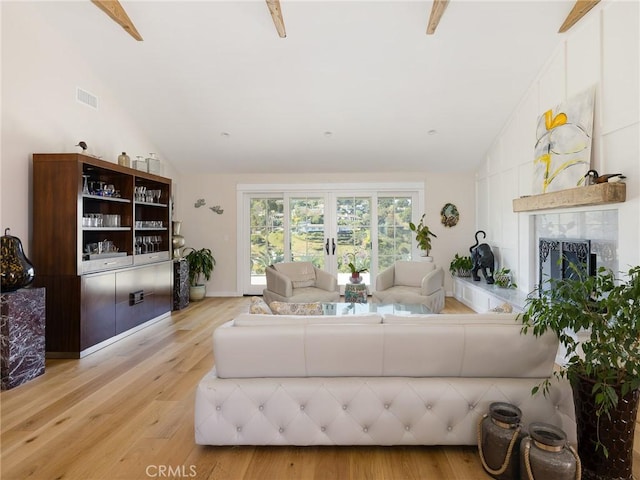 living area featuring high vaulted ceiling, visible vents, a tiled fireplace, and light wood finished floors