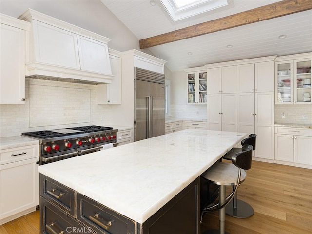 kitchen with vaulted ceiling with skylight, white cabinetry, high quality appliances, a center island, and glass insert cabinets